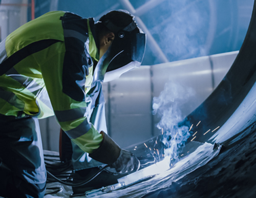 welder wearing mask and using a welder in a large tube